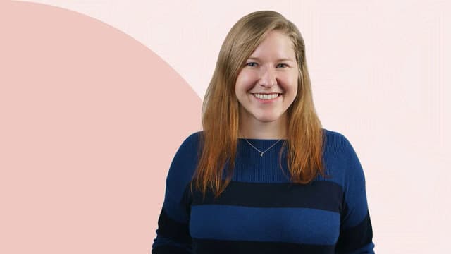 Woman in blue and black striped shirt smiling on a pink background
