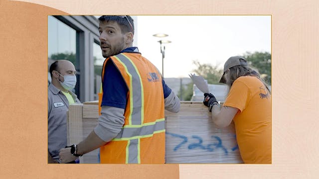 Man in orange vest turning around while employees work beside him